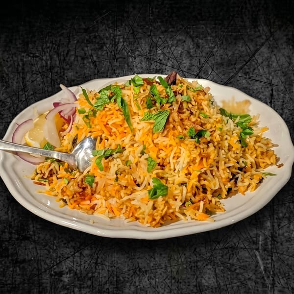 A white plate filled with colorful biryani rice, garnished with fresh mint, red onions, and lemon wedges.