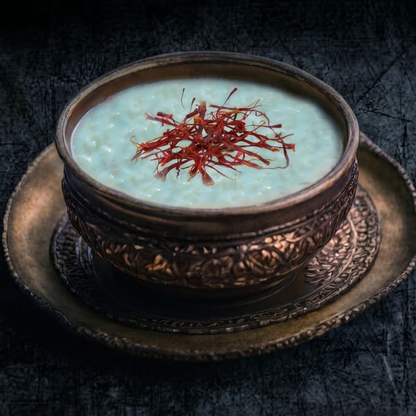 A bronze bowl of creamy rice pudding, topped with vibrant red saffron threads, on a matching plate.
