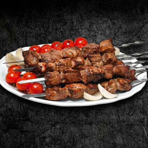 Grilled meat skewers with cherry tomatoes and onion slices on a white platter.