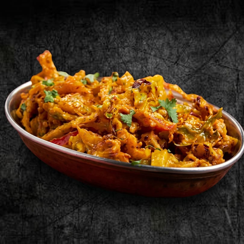 Close-up of a copper bowl filled with vibrant orange pakora, garnished with fresh cilantro.